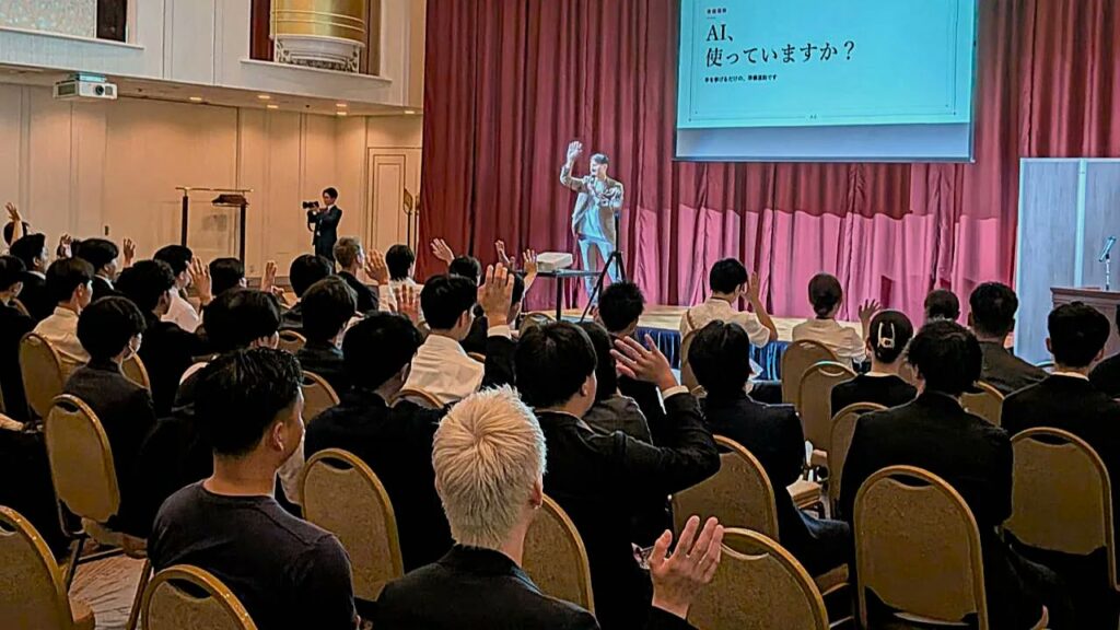 「AI、使っていますか?」のスライドの前で話す赤堀と、手を挙げる参加者